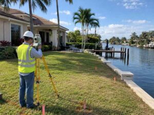 Residential land survey in Miramar Florida showing a surveyor measuring a canal-adjacent home with a seawall and private dock